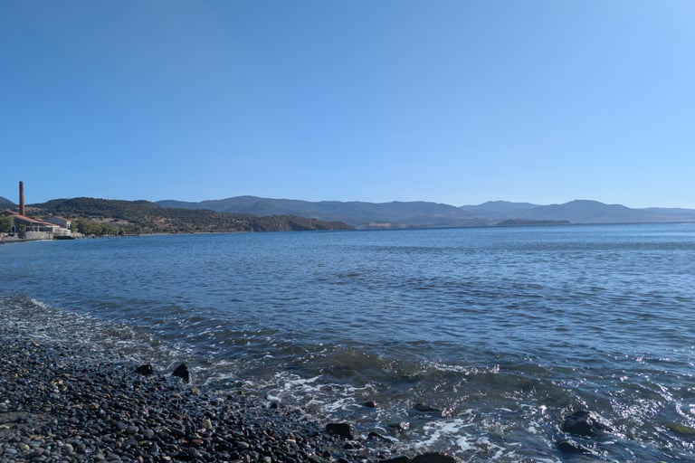 the rocky shore and blue water of the Aegean Sea at Paralia Molivos beach in Petra, Greece