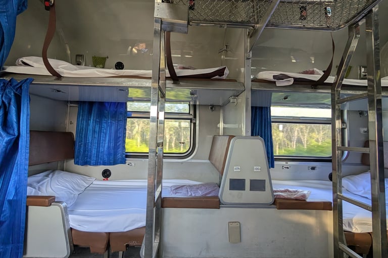 Interior of a sleeper train cabin featuring multi-level bunk beds with white linens and blue curtains.