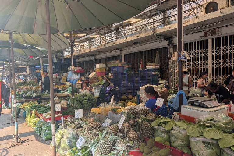 street market in Thailand selling fresh pineapples, bananas, and tropical vegetables under green umbrellas.