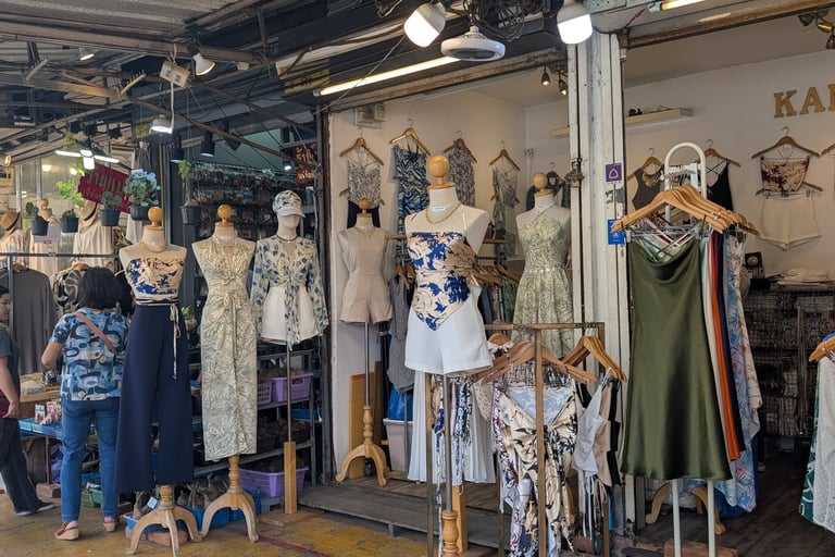 A women's clothing boutique in a market featuring floral dresses and stylish outfits on mannequins.