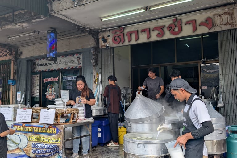 Street food vendors preparing steamed dishes in large metal pots at an authentic Thai food stall.