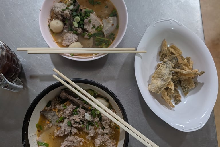 Two bowls of Thai pork noodle soup with fish balls and a side of crispy fried fish skin.