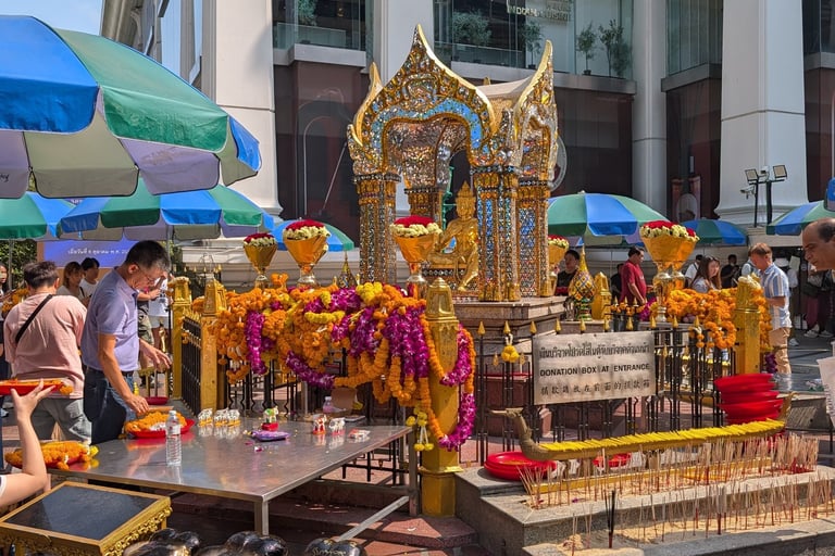 People praying at the Erawan Shrine in Bangkok with flower garlands and incense offerings.