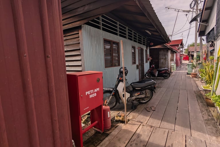 A narrow wooden boardwalk pathway in a Malaysian Yeoh Jetty with stilt houses and parked motorbik