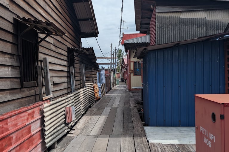 A narrow wooden boardwalk path between traditional rustic houses in a floating stilt village. Yeoh Jetty