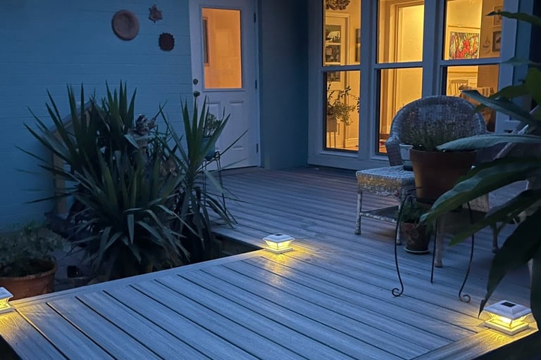 Illuminated modern composite deck with solar post cap lights in a backyard at dusk.