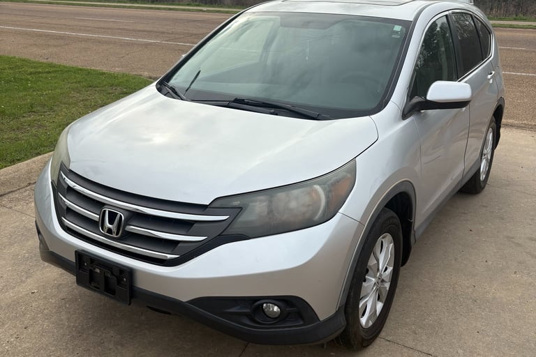 Silver Honda CR-V compact SUV parked on a concrete driveway with trees in the background.
