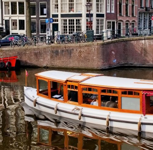 A classic wooden canal boat cruising past historic buildings and parked bicycles in Amsterdam.