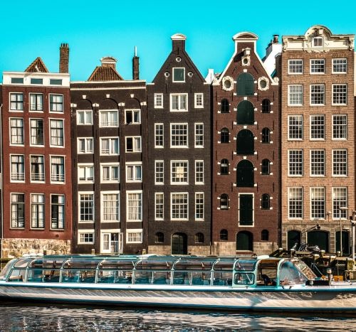 Historic Dutch canal houses in Amsterdam with a glass-top tour boat cruising the water.