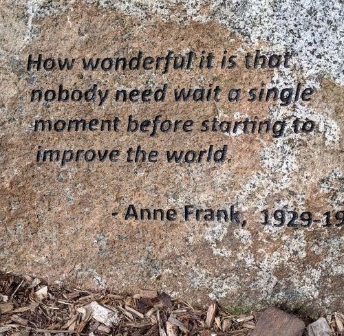Inspirational Anne Frank quote engraved on a large stone monument over wood chip mulch.