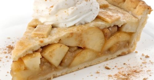 A slice of homemade apple pie with a lattice crust topped with whipped cream and cinnamon.