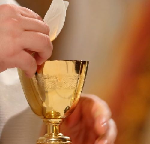 a catholic priest holding a golden cup with wine