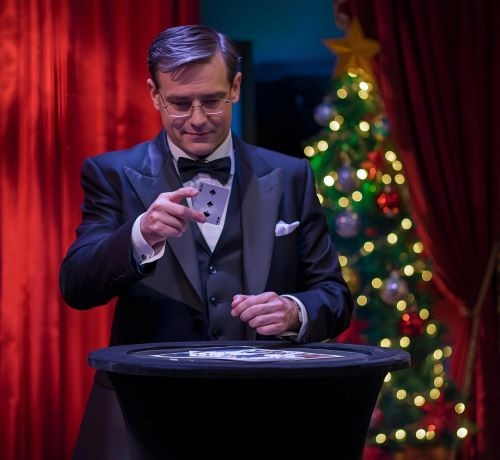a magician doing a cart tric with a christmas tree in the background