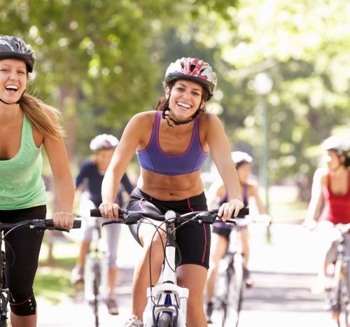 two women riding bikes on a path in a park