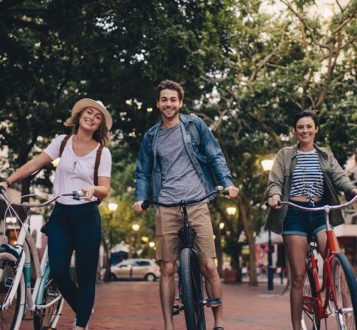 Three smiling friends riding bicycles down a tree-lined city street during a summer bike tour.