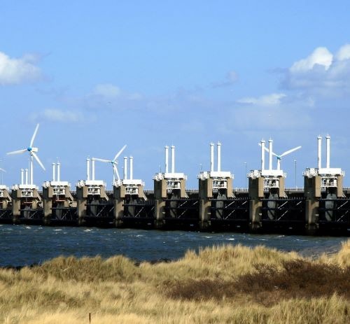 The Oosterscheldekering storm surge barrier in the Netherlands with wind turbines under a blue sky.