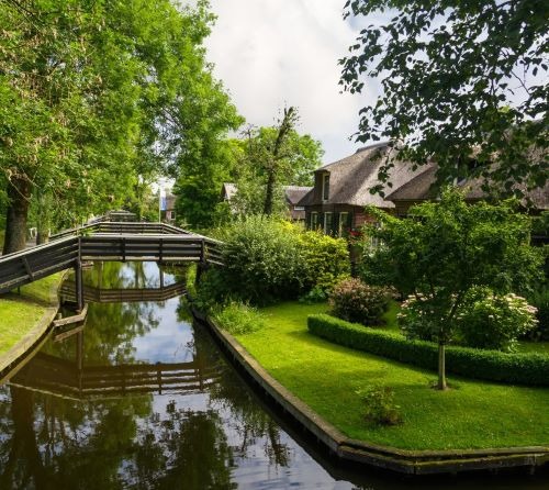 Scenic canal in Giethoorn, Netherlands, with thatched-roof houses and wooden footbridges.