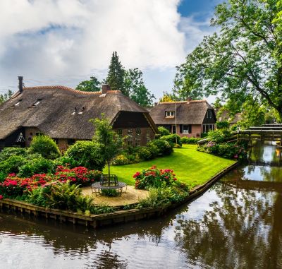 Charming thatched-roof cottages and blooming gardens along a canal in Giethoorn village.