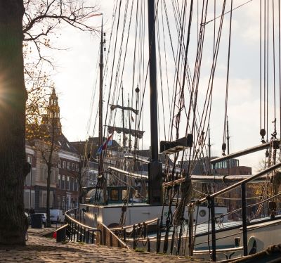 Historic Dutch tall ships with rigging docked in a sunny canal harbor in Groningen, Netherlands.