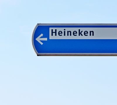 a blue street sign - with heineken on it - an arrow pointing to the left