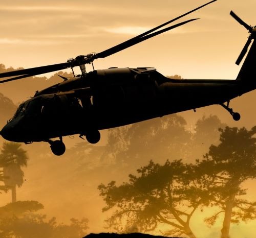 a helicopter flying over a hill with trees in the background