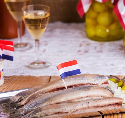 Traditional Dutch soused herring served with onions and Dutch flag toothpicks alongside white wine.