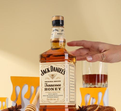 a person holding a bottle of whiskey and a glass of honey
