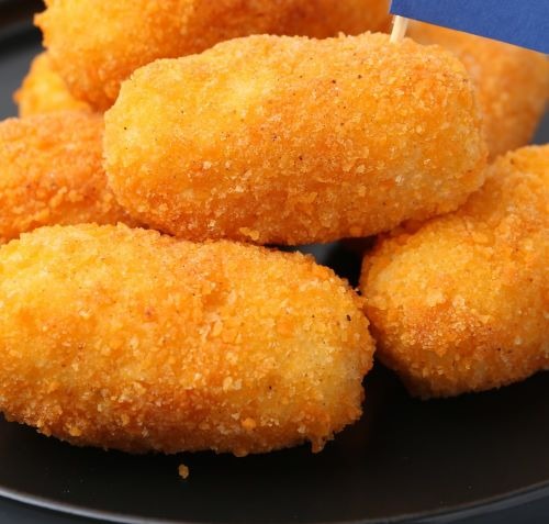 Golden brown crispy potato croquettes served on a black plate, close-up shot.