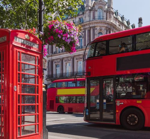 a red double decker busses parked next to a red phone booth