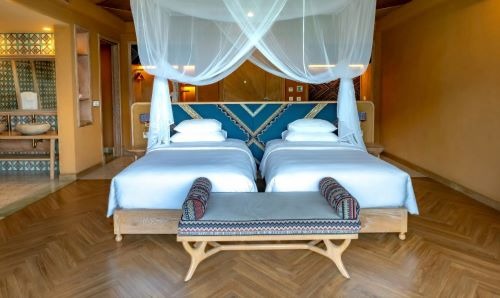 a hotel bedroom with two beds and a bench