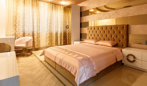 Luxury modern bedroom with a tufted headboard, pink bedding, and elegant gold patterned curtains.