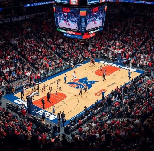 A crowded indoor basketball arena during a professional game with fans in red seating.