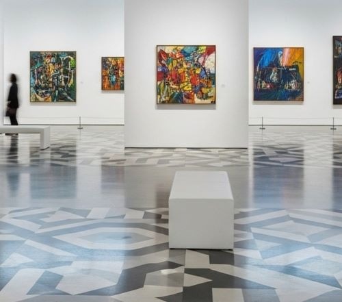 Modern art gallery with abstract colorful paintings displayed on white walls above patterned floors.