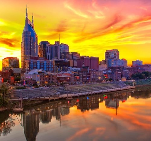 Nashville skyline reflecting in the Cumberland River during a vibrant orange and yellow sunset.
