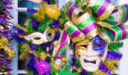 Festive Mardi Gras wreath featuring purple, green, and gold tinsel, ribbons, and theater masks.