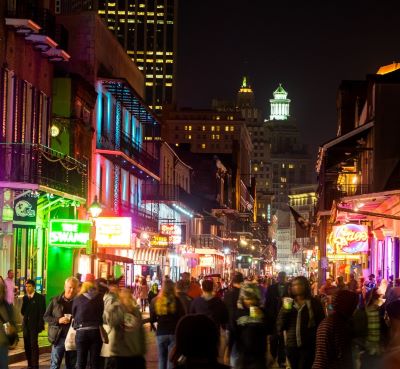 Crowded Bourbon Street at night with bright neon signs and historic French Quarter architecture in New Orleans.