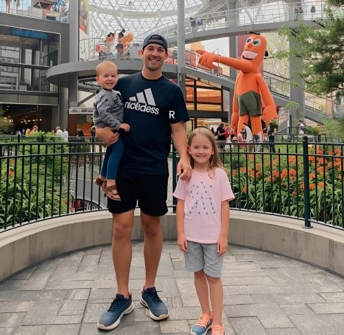 a man and two children standing in front of a giant orange in a mall