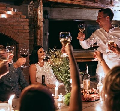 Smiling friends toast with wine glasses during a cozy candlelit dinner party in a rustic cellar.