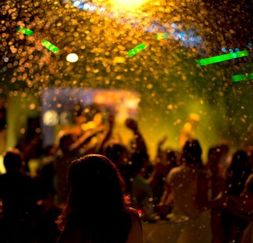 Crowd dancing at a night club party with golden confetti and glowing bokeh lights.