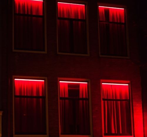 Red light district windows with glowing neon lights and red curtains at night.