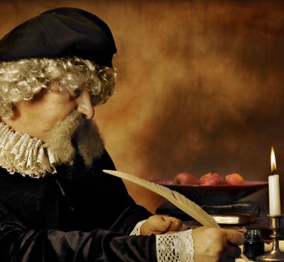 A man in a Renaissance costume writing with a quill pen by candlelight.