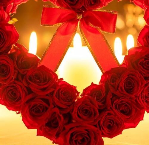 a heart shaped wreath made of roses and candles