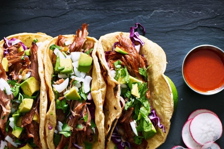 a group of three tacos with a bowl of sauce and a bowl of sauce