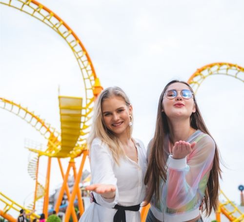 two women standing next to each other in front of a roller coaster