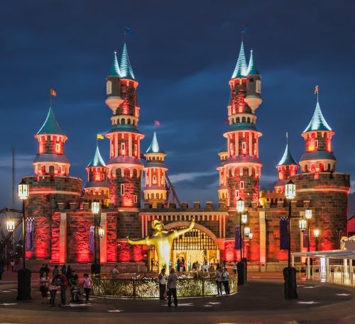 a fairytale castle in a theme park with a clock tower in the middle of it