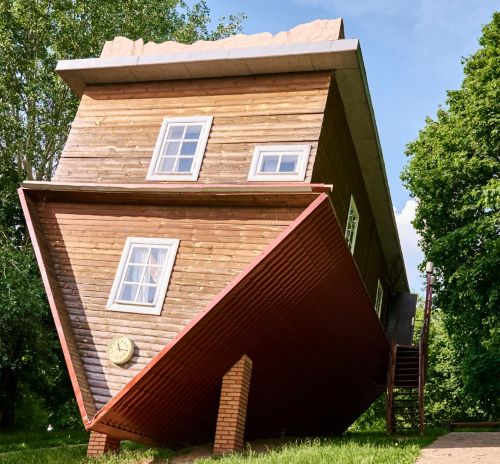 A wooden upside-down house tourist attraction standing on its roof in a green park.