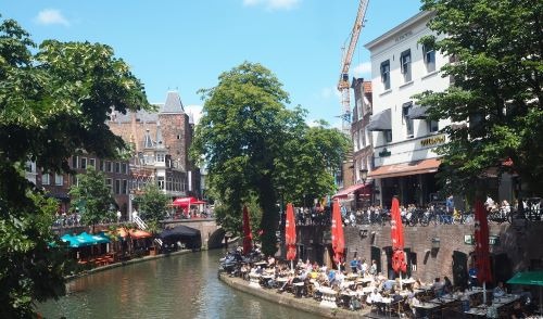 a river with people sitting at tables close to a canal in utrecht