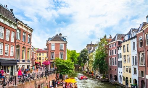 Historic canalside buildings and bustling boat traffic under a blue sky in Utrecht, Netherlands, showcasing the vibrant city