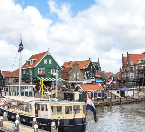 Traditional green wooden houses and tourist boat at Volendam harbor in the Netherlands.