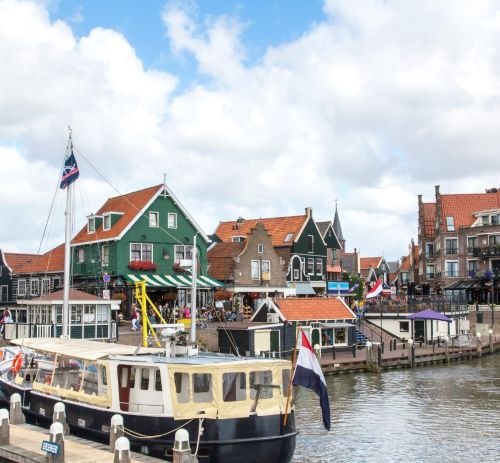 Traditional Dutch houses and boats in the historic Volendam harbor under a cloudy sky.